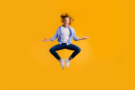 Full length photo of redhead handsome guy jumping high meditating exercise holding body in lotus position wear casual trendy clothes isolated yellow backgroundの写真素材