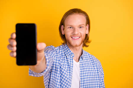 Photo of cheerful handsome promoter presenting new model of telephone smiling toothily wearing...