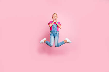 Full length body size photo of nice cute rejoicing overjoyed childish girl wearing jeans denim overall fuchsia t-shirt jumping up seeing sales isolated over pink pastel color backgroundの写真素材