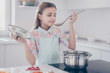 Close-up portrait of her she nice attractive beautiful charming lovely cute dreamy pre-teen girl making useful hot dish tasting homemade tradition in light white interior kitchen house indoorsの写真素材