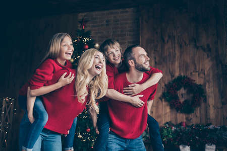 Photo of full four members family daddy mommy sister brother spending x-mas time together holding piggyback indoors waiting relatives reunion visit wear red jumpersの写真素材