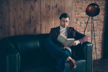 Photo of macho business guy holding hands corporate book reading, article about famous chiefs wear specs stylish blazer turtleneck sitting couch modern officeの写真素材