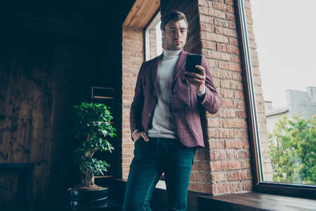 Photo of luxury macho business guy looking telephone read company email wear, stylish blazer turtleneck leaning wall window modern office roomの写真素材