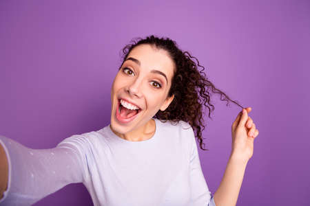 Self-portrait of her she nice attractive lovely pretty cheerful cheery ecstatic amazed wavy-haired girl playing with curl having fun isolated over violet lilac purple pastel color backgroundの写真素材