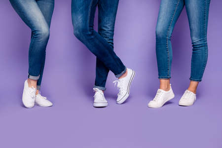 Cropped closeup photo of three peoples legs wearing denim dark blue jeans trousers pants standing on the floor isolated violet backgroundの写真素材
