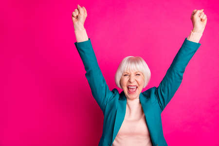 Portrait of her she nice attractive cheerful cheery overjoyed gray-haired lady wearing blue green jacket rejoicing rising hands up isolated on bright vivid shine vibrant pink fuchsia color backgroundの写真素材