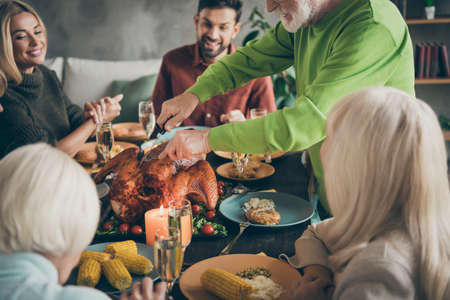Cropped photo of full big family sit feast dishes table around roasted turkey grandfather cutting meat into slices hungry relatives waiting excited in living room indoorsの写真素材