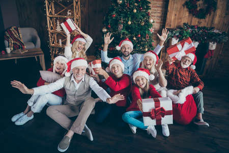 Portrait of nice lovely cheerful big full family brother sister couples wearing cap hat headwear sitting on floor holding in hands gifts waving hi hello tradition loft industrial style interior houseの写真素材