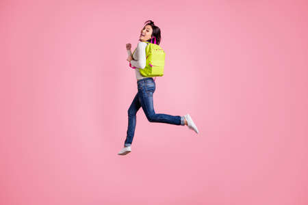 Full body photo of crazy lady jumping high holding green rucksack running autumn sale shopping wear pullover and jeans isolated pink color backgroundの写真素材