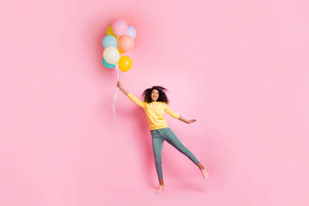 Full length photo of funky childish dreamy african girl hold many balons try fly in air enjoy holidays, anniversary wear good look outfit sneakers isolated over pink color backgroundの写真素材