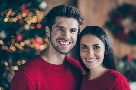 Close up photo of charming romantic couple with brunette hair enjoying, christmas night x-mas holidays wearing red pullover in room with illumination newyear lights indoorsの写真素材