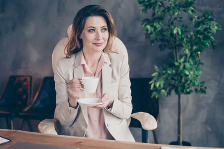 Close-up portrait of her she nice attractive stylish cheerful dreamy, mature lady having pause drinking espresso beverage at industrial style interior indoors work place stationの写真素材