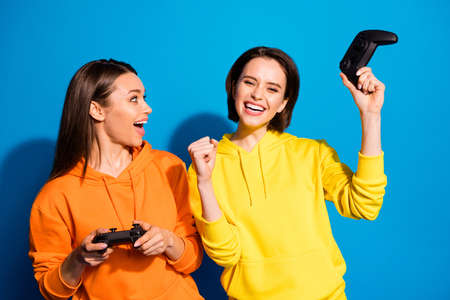 Photo of two funny two ladies holding in hands joystick playing video game, rejoicing after win wear...