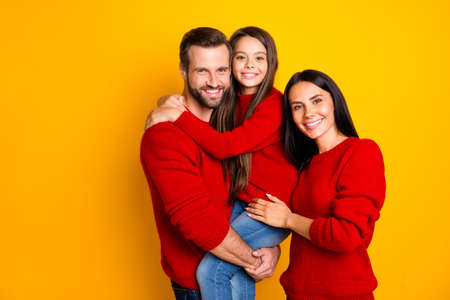 Photo of funky day toothy nice fascinating family with kid wearing jeans denim red sweater father holding daughter with hands mother embracing isolated over vivid color backgroundの写真素材