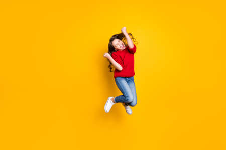 Full size photo of delighted crazy child wavy curly hair lucky kid win contest raise fists scream yeah wear stylish trendy pullover white sneakers isolated over yellow color backgroundの写真素材