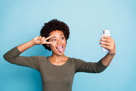 Photo of cute cheerful nice attractive black skinned woman fooling, before camera showing v-sign...