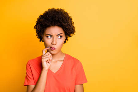 Photo of funny dark skin lady doubtful about making important decision, wear orange v neck t-shirt isolated yellow color backgroundの写真素材