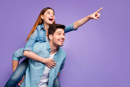 Portrait of enthusiastic two students couple of sweethearts have date point index finger at copyspace hug piggyback wear stylish clothes isolated over purple violet color backgroundの写真素材