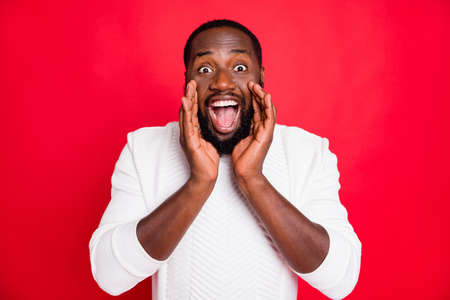 Hey listen new promo. Portrait of crazy funky african man hold hand near mouth shout ads share confidential information wear style white sweater isolated over red color backgroundの写真素材