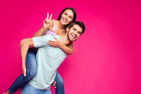 Photo of funny carefree guy and lady holding piggyback showing v-sign, symbol wear casual clothes isolated vivid pink color backgroundの写真素材
