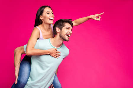 Photo of funny guy and lady holding piggyback looking empty space, indicating finger pretty park to go wear casual clothes isolated vivid pink color backgroundの写真素材