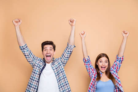 Portrait of his he her she nice attractive lovely satisfied ecstatic glad, cheerful cheery couple wearing checked shirt celebrating rising hands up isolated over beige pastel color backgroundの写真素材