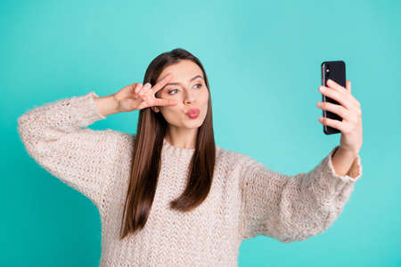 Portrait of charming lovely girl make selfie v-signs send air kisses to her blog followers wear white knitted pullover jumper isolated over teal turquoise color backgroundの写真素材