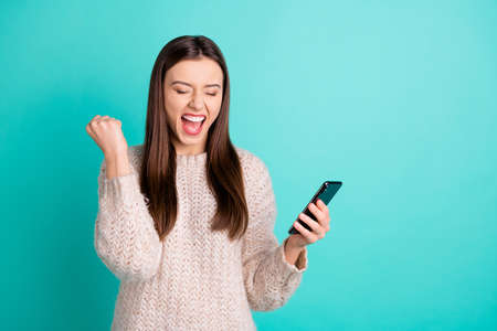 Portrait of cheerful delighted girl read news from her cell phone scream yeah raise fists isolated over teal turquoise color backgroundの写真素材