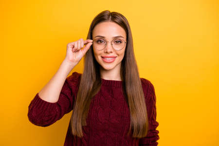 Portrait of charming lady touching her specs smiling wearing marsala pullover isolated over yellow backgroundの写真素材