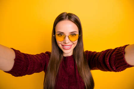 Close up photo of cheerful girl making photo smiling wearing marsala pullover isolated over yellow backgroundの写真素材