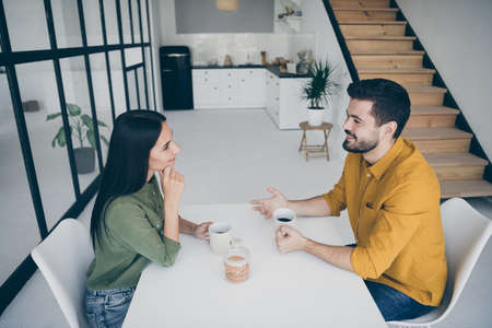 Profile photo of handsome guy and his pretty lady drinking hot beverage sitting chairs opposite in...