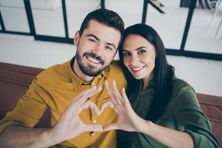 Close up photo of handsome guy and his wife lady moving to first flat as married people showing heart figure with arms in modern flat indoors wear casual clothesの写真素材