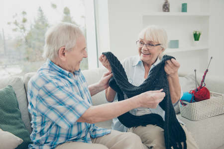 Portrait of his he her she two nice cheerful cheery people life partners sitting on divan granny giving new scarf to granddad in light white interior living-room house indoorsの写真素材