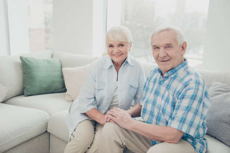 Portrait of two nice attractive lovely cheerful cheery person spouses holding hands sitting on divan spending time in light white interior living-room indoorsの写真素材
