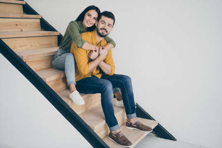 Full body profile photo of handsome guy and his pretty lady sitting comfy on stairs in modern room...