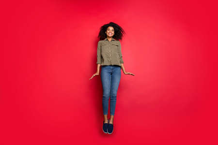 Full length body size photo of cheerful positive cute youngster wearing jeans denim shirt footwear jumping up isolated over vivid color backgroundの写真素材