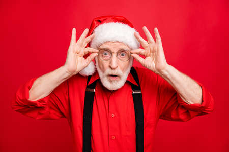 Close-up portrait of his he nice amazed stunned speechless bearded Santa showing omg expression touching specs looking isolated over bright vivid shine vibrant red backgroundの写真素材