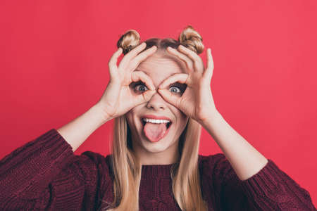 Closeup photo of pretty lady showing okey symbols near eyes in specs form sticking tongue out mouth wear knitted pullover isolated pastel red color backgroundの写真素材