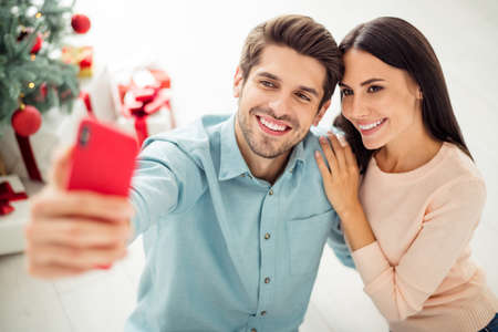 Close up photo of two people cheerful spouses making selfie on cell phone sitting on floor enjoy christmas time x-mas holidays in house indoorsの写真素材