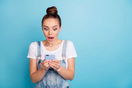 Photo of girlfriend amazedly staring at her phone screen seeing something incredible while isolated with blue backgroundの写真素材