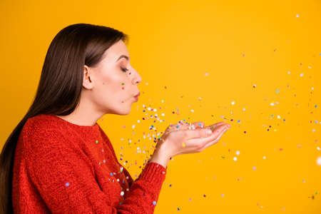 Photo of cute sweet charming nice girl blowing confetti away from her hands with eyes closed...