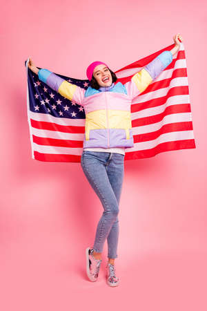 Pretty lady making photos with usa flag glad to visit new country wear warm colored coat isolated pink backgroundの写真素材