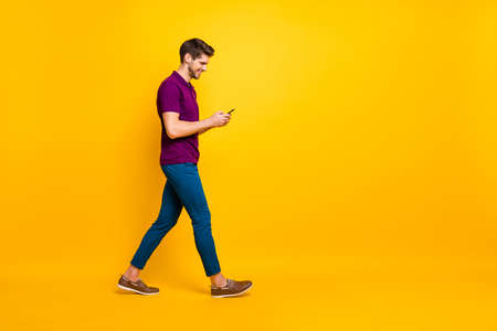 Full length body size profile side view of his he nice attractive cheerful cheery glad addicted guy using digital device 5g smm walking, isolated over bright vivid shine vibrant yellow color backgroundの写真素材