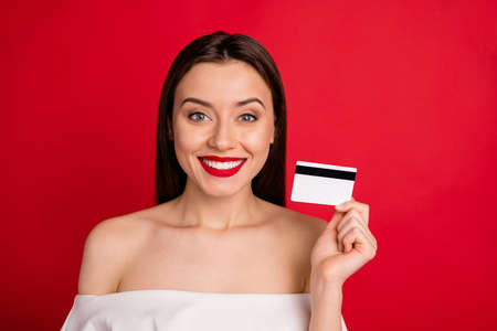 Close up photo of attractive, lady with toothy smile holding credit card isolated over red backgroundの写真素材