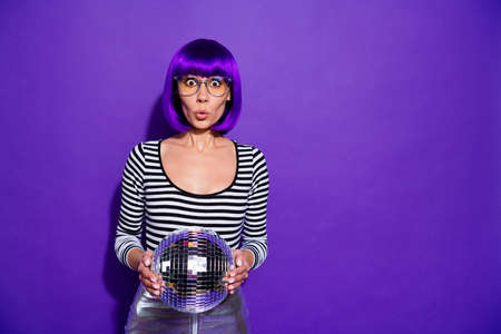 Portrait of impressed lady with eyewear eyeglasses holding mirror ball isolated over purple, violet backgroundの写真素材