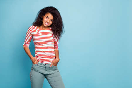 Photo of amazing pretty dark skin lady with adorable smile holding hands in pockets wear casual street clothes isolated pastel blue color backgroundの写真素材