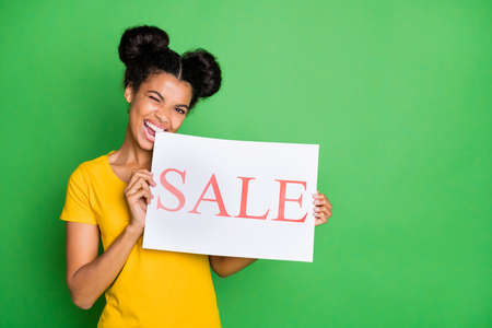 Photo of amazing dark skin lady holding and biting placard with black friday prices inviting customers to visit season sale wear casual yellow t-shirt isolated green backgroundの写真素材