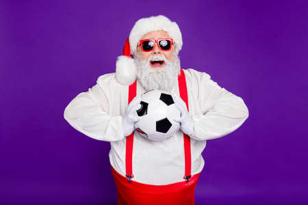 Photo of grey haired santa father holding football ball spend newyear night watching champion league excited final game wear sun specs costume isolated purple backgroundの写真素材