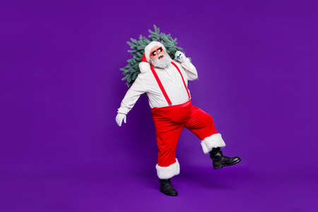 Let it snow. Full length photo of funny fat santa father holding x-mas tree on shoulder wanna make perfect eve wear sun specs costume isolated purple backgroundの写真素材