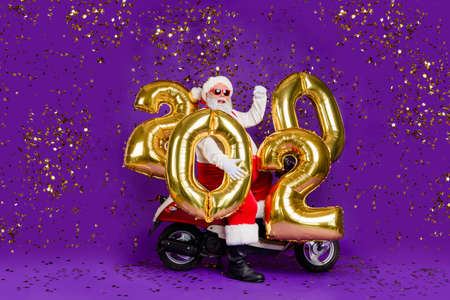 Full body photo of fat santa man sitting on bike carry newyear 2020 numbers balloons confetti...